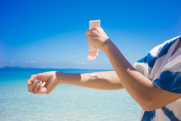 A person applying sunscreen on their arm while wearing a wide-brimmed hat and sunglasses. The beach is in the background, with clear blue water and a sunny sky.
