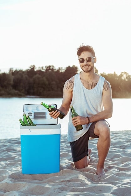 A cooler filled with ice, water bottles, fresh fruits, and healthy snacks. The cooler is sitting on a beach towel next to a beach chair.