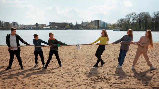 Two teams of adults engaged in a tug-of-war game on the beach, pulling with all their might as their teammates cheer them on. The image highlights the intensity and fun of the competition.