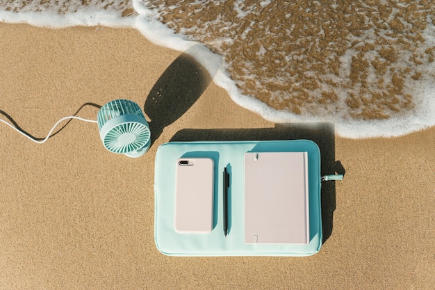 A waterproof floating pouch with a clear window is displayed on a beach towel. Inside the pouch, a smartphone, keys, and a small wallet are visible. The pouch is sealed tightly, and droplets of water are visible on its surface.