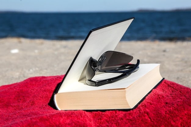 A hollowed-out book with a cutout compartment sits on a beach towel. Inside the compartment, keys, cash, and a small pair of earrings are visible. The book is surrounded by sunglasses, a beach umbrella, and a bottle of sunscreen.