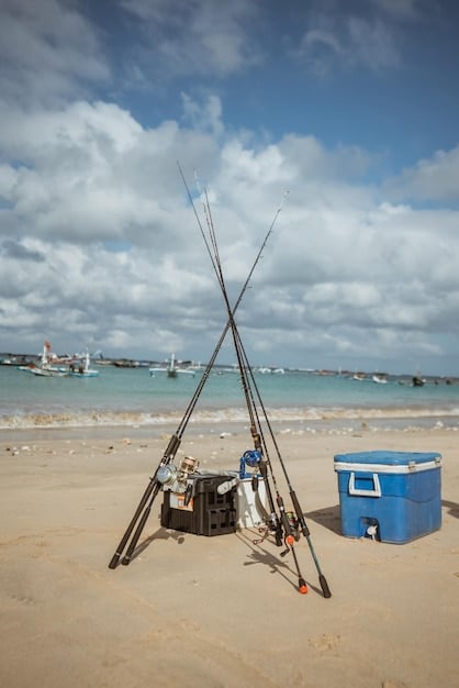 A medium shot of a beach fishing setup, including a sand spike rod holder, tackle box, and a cooler on the sand, with the ocean in the background. The scene is peaceful and inviting.