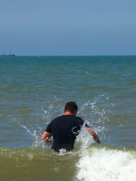 A bodyboarder paddles efficiently on a wave, showcasing proper technique and body positioning, with a clear view of the water and horizon.