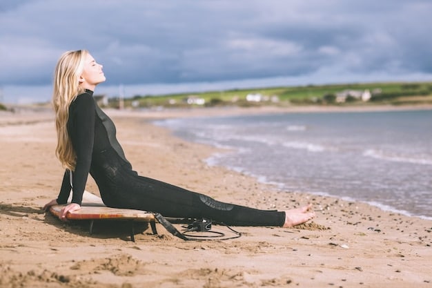 A surfer is performing a seated forward fold (Paschimottanasana) on a beach at sunrise. The pose highlights hamstring and back flexibility, essential for surfers duck diving under waves.