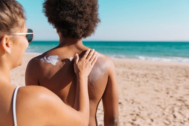 A person applying sunscreen to another person's back at the beach. The ocean is visible in the background.