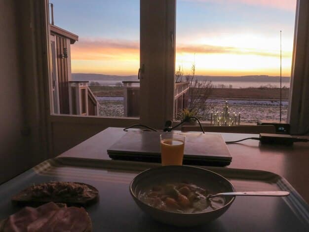 A cozy and well-decorated vacation rental apartment with a balcony overlooking a calm beach at sunset. The scene suggests a comfortable and affordable accommodation option for a budget beach vacation.