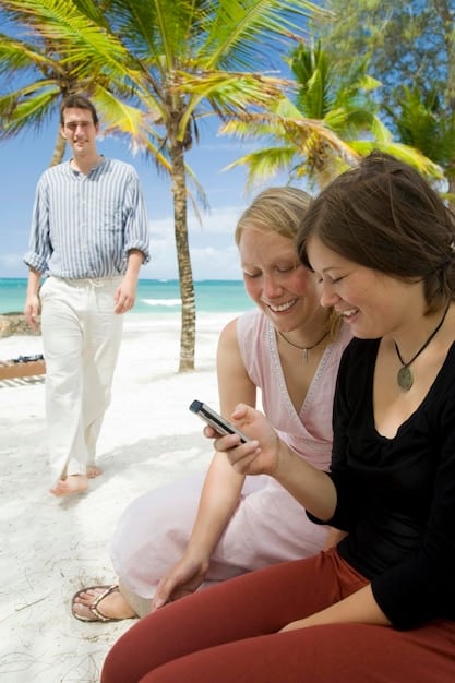 A group of guests at a luxury beach resort receiving instructions from a certified scuba diving instructor. The instructor is demonstrating the use of scuba gear, and the guests are attentively listening. The background shows clear blue water and a dive boat.