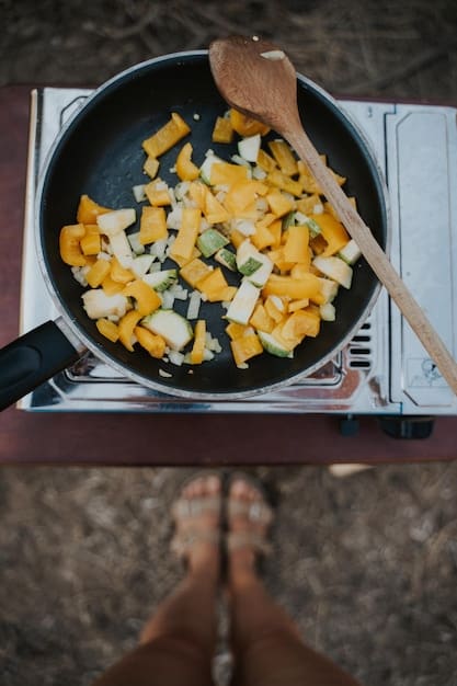 A close-up shot of a simple, well-organized beach campsite cooking setup, featuring a portable stove, basic cookware, and ingredients for a budget-friendly meal like pasta with vegetables.