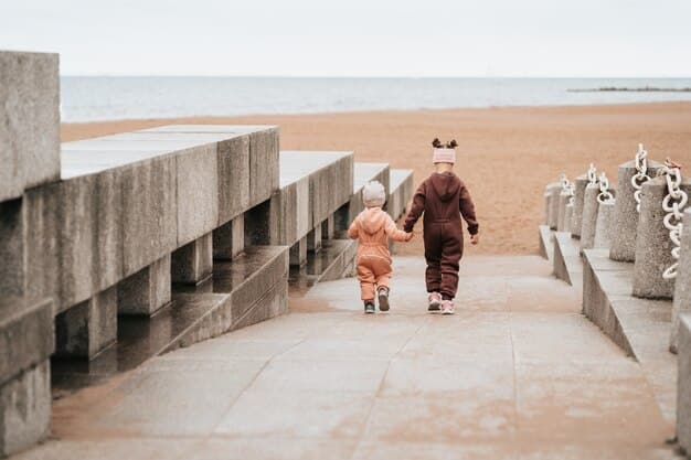 A family of four walks along a less-crowded beach in the Outer Banks, North Carolina, at sunset. The sky is painted with orange and pink hues, and the ocean reflects the warm light.  A beach house is visible in the distance.