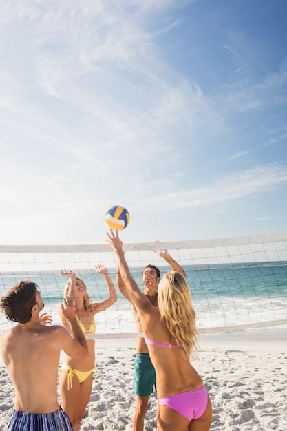 A group of friends playing beach volleyball on a sunny day, with the ocean and clear sky in the background.