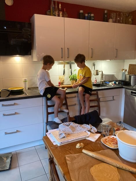 A family preparing a meal together in a vacation rental kitchen. The scene is warm and inviting, with natural light streaming through the window. The family is smiling and enjoying the cooking process.