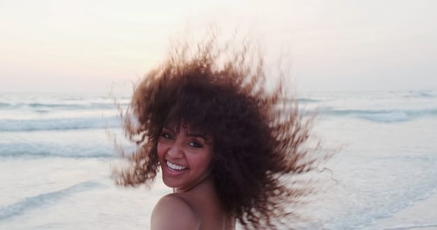 A close-up of a woman's perfect beach waves, achieved with a protective hairstyle, with the ocean blurred in the background.