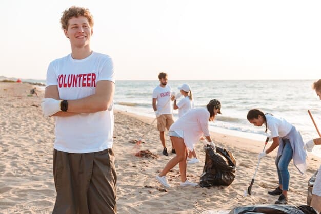 A group of volunteers in matching t-shirts, enthusiastically participating in a beach clean-up, picking up small pieces of plastic from the sand with a backdrop of a clean, sunny beach.