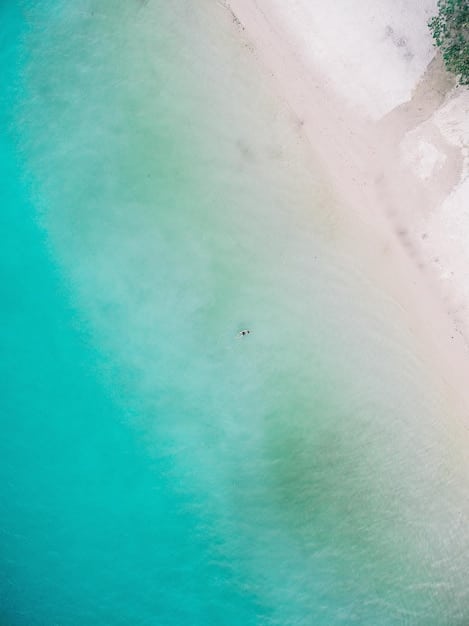 A serene aerial shot of a tranquil beach with clear turquoise water gently lapping a pristine white sandy shore, with no people visible, emphasizing the untouched beauty and calming atmosphere.
