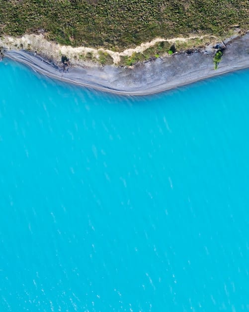 An overhead drone shot of a beach showing a clear, calm channel of water extending from the shore through the breaking waves, contrasting with the choppy water on either side, illustrating a visible rip current.