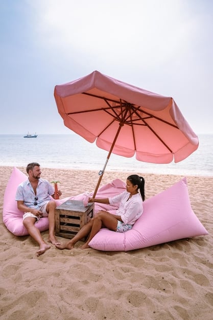 A family relaxing under a large beach umbrella, enjoying the shade while the sun brightly illuminates the beach in the background.