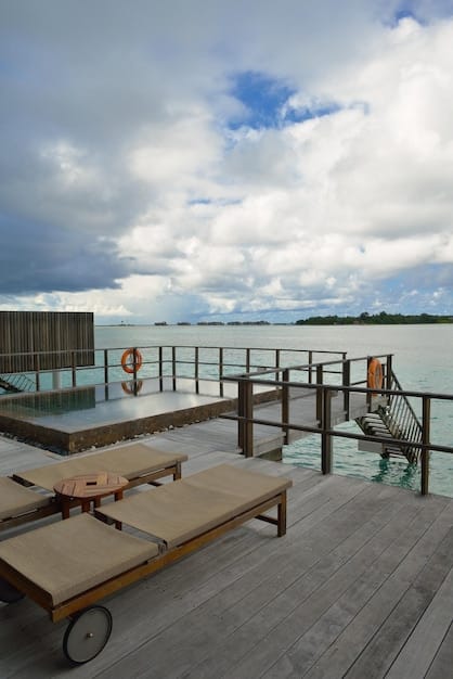 An elegant overwater bungalow at The St. Regis Bora Bora Resort, with a private deck extending over the clear turquoise lagoon, mountains in the distance, and the early morning sun casting a warm glow.