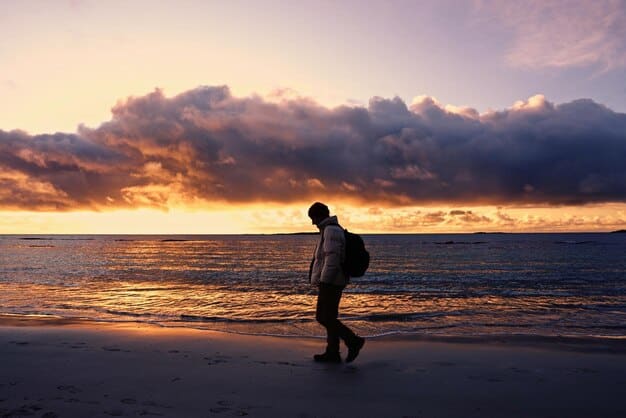 A person happily walking along a quiet stretch of beach during sunset, carrying a small backpack, symbolizing independent and extended travel.