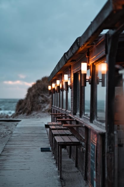 A tranquil, less-crowded beach town boardwalk at dusk, with cozy, affordable-looking motels and local eateries visible against a warm sunset, suggesting a peaceful budget vacation.