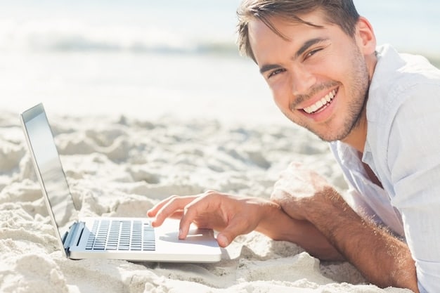 A person happily typing on a laptop with a beachfront backdrop, showcasing various loyalty cards and discount memberships scattered around, symbolizing smart booking and savings.