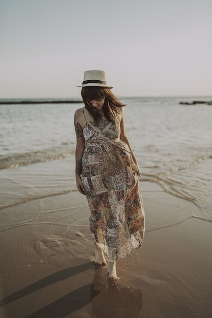 A chic woman wearing a wide-brimmed hat and a stylish, quick-drying cover-up, walking along a sunny beach with the ocean in the background, embodying fashion and function.