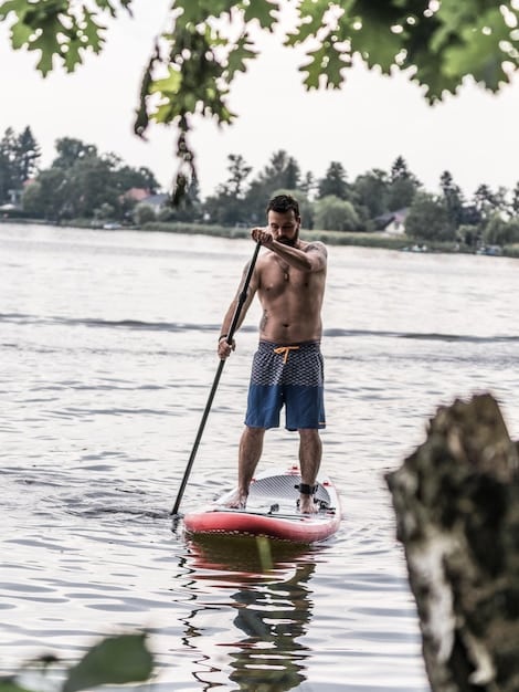 A paddleboarder demonstrates good core engagement, standing tall and using their whole body to power the stroke, on a sunny day with clear water.