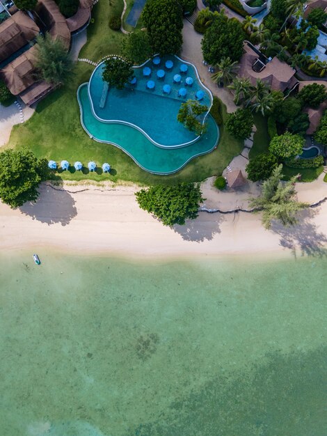 An aerial view of a sprawling luxury resort on a tropical coastline, showing multiple pools, lush gardens, and a pristine private beach.